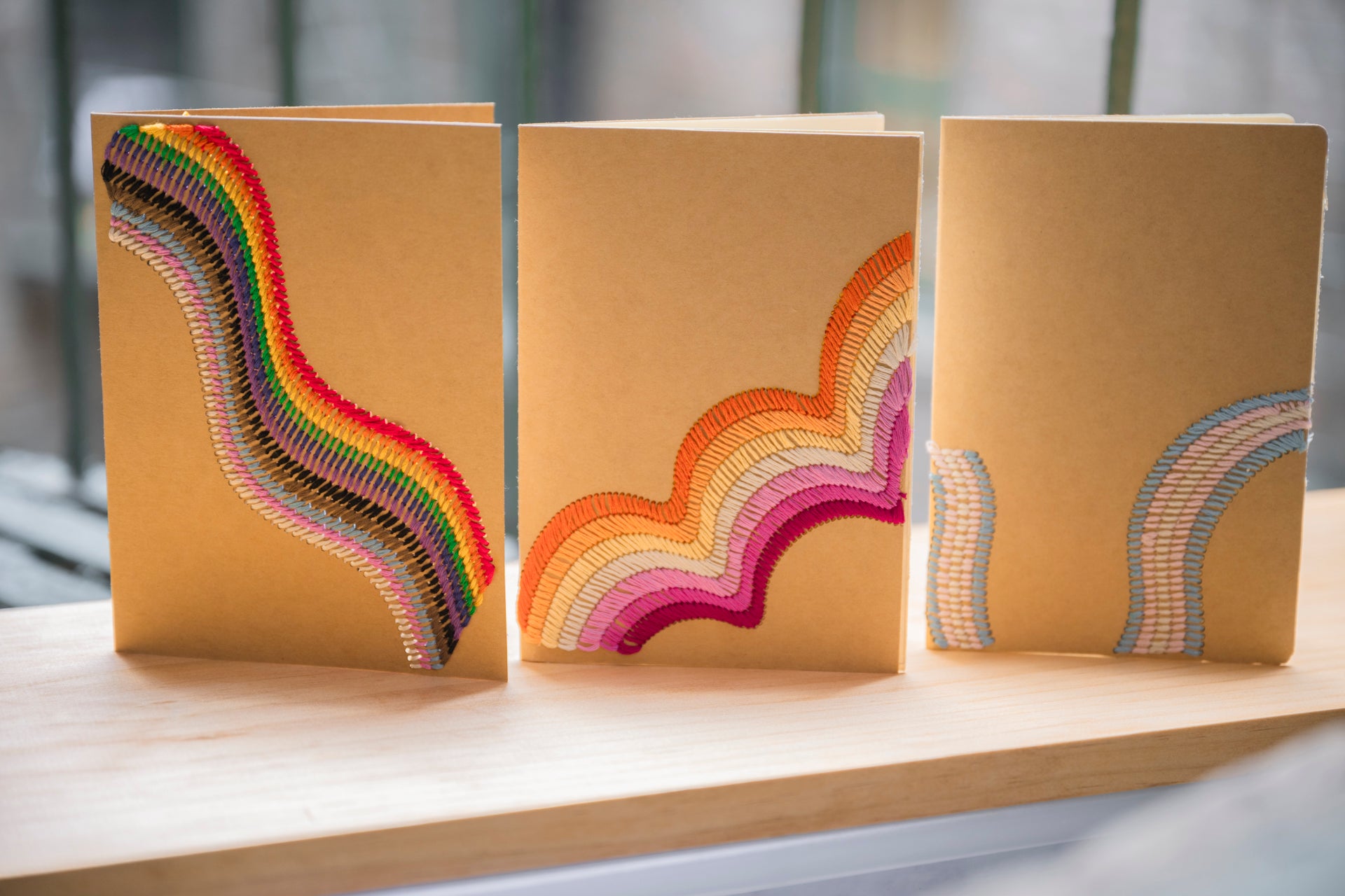 Three individual cards with wavy patterns of different LGBTQ+ Pride flags. From left to right: Rainbow flag, lesbian flag, trans flag.